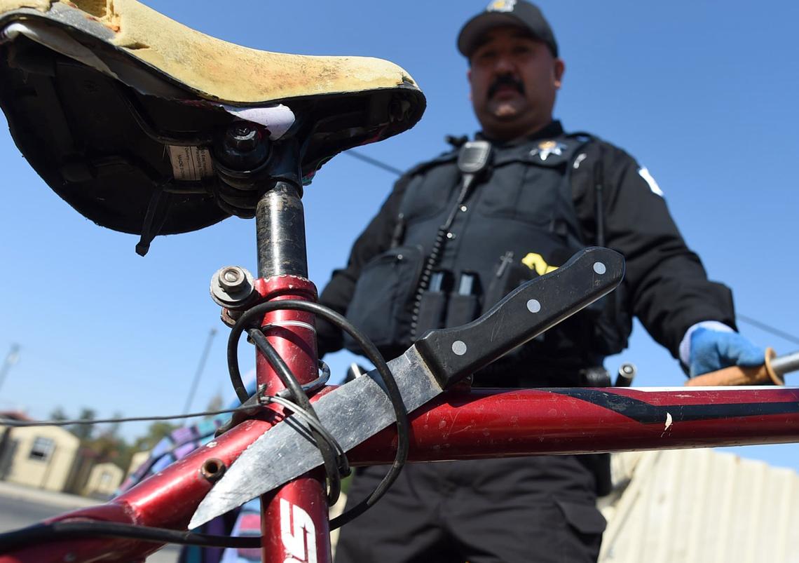 Officer Joel Sanchez shows a large-bladed knife attached to a bike found in an unattended homeless camp during a cleanup along G Street on Wednesday morning, Aug. 14, 2018.