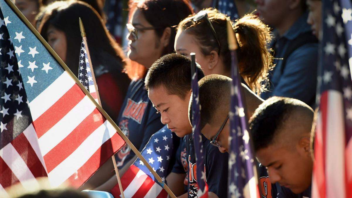 The early-morning sun falls upon Duncan Polytechnical High School freshman Daniel Yang at center, and other students who bow their heads during the ceremony in remembrance of the 9/11 tragedy, flanked by Duncan students holding flags, Sept. 11, 2018.
