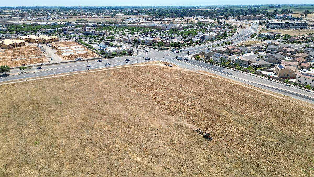 A tractor works in a large empty lot across from businesses in the Marketplace at El Paseo shopping center in northwest Fresno. The lot has been designated to be Fresno's largest Costco but zoning and environmental analysis setbacks have delayed the project.