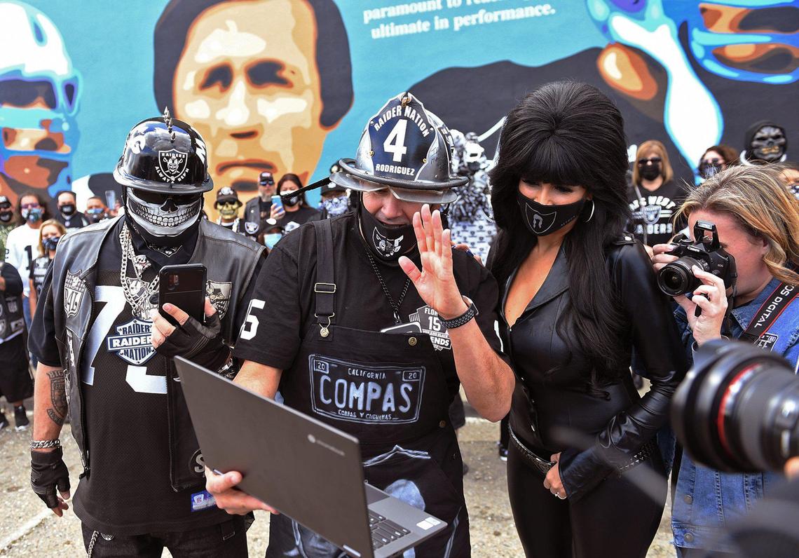 Polo Rodriguez, center, waves as and other Raiders fans greeting Tom Flores on a Zoom call gather in front of a mural honoring Flores Saturday, Feb. 20, 2021 in downtown Sanger.