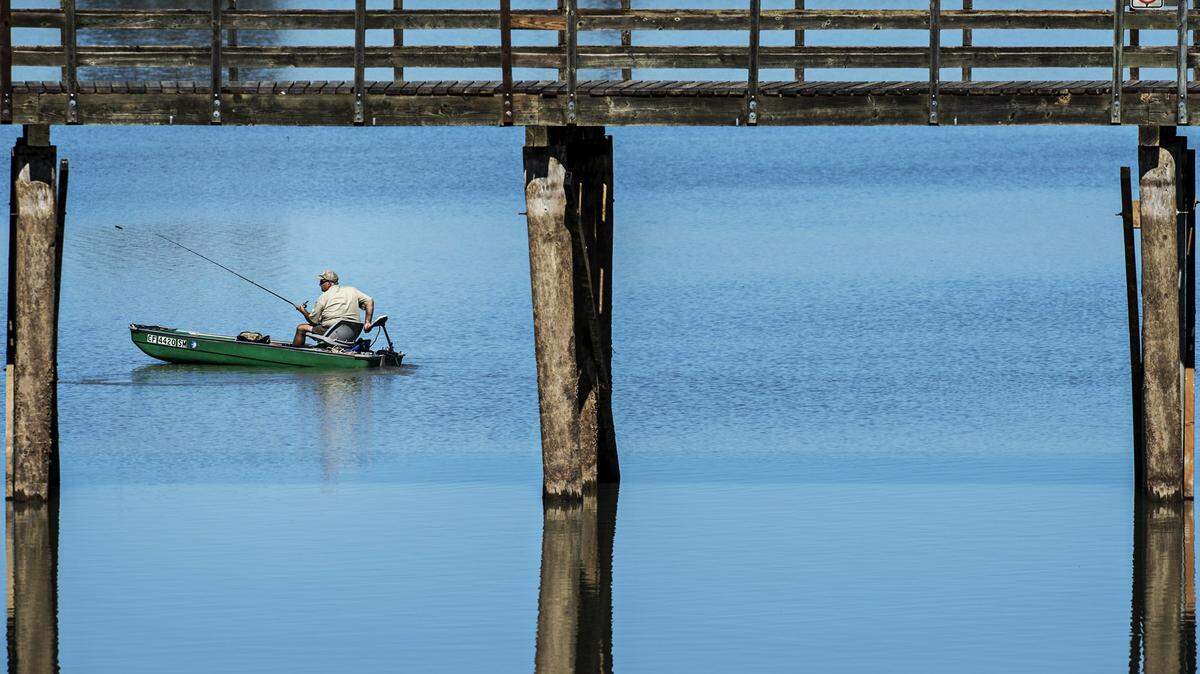 A man fishes from a boat near the Lake Yosemite pier in Merced, Calif.