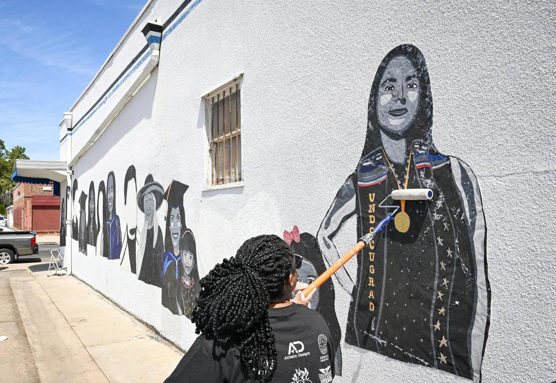 Muralist Nelly Ferol uses a paint roller to affix a mural print to the wall of the Fulton Studios building at Fulton and the 180 freeway in Fresno on Saturday, June 14, 2025.
