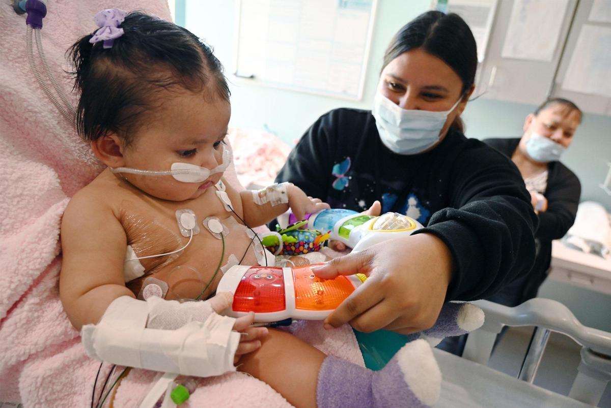 Wendy Batres, center, plays with her daughter Victoria Saypen, left, who developed respiratory syncytial virus, or RSV, and was treated at Valley Children’s Hospital’s ICU. A breathing tube was used for a few weeks and she developed complications from a small bowel perforation, but she is doing well and was expected to be released within days. Photographed at Valley Children’s Hospital, Thursday, March 2, 2023 in Madera County.