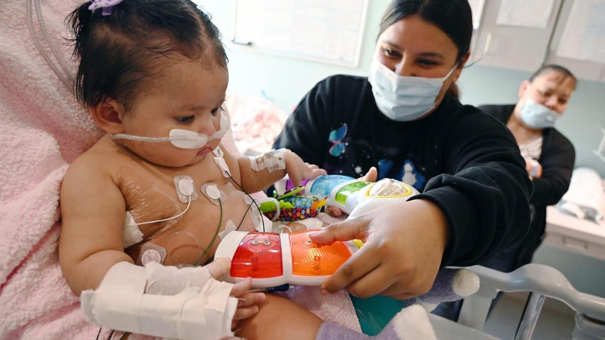 Wendy Batres, center, plays with her daughter Victoria Saypen, left, who developed respiratory syncytial virus, or RSV, and was treated at Valley Children’s Hospital’s ICU. A breathing tube was used for a few weeks and she developed complications from a small bowel perforation, but she is doing well and was expected to be released within days. Photographed at Valley Children’s Hospital, Thursday, March 2, 2023 in Madera County.
