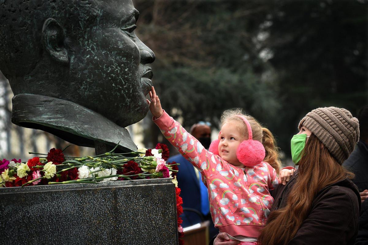4 1/2-year-old Evelee Swint reaches out to touch the bronze bust of Rev. Dr. Martin Luther King, Jr., held by her mother Kyla Mitchell, after the garlanding ceremonies to the kick off the 38th annual events to remember and honor the slain civil rights leader, at Courthouse Park, Friday Jan. 14, 2022.