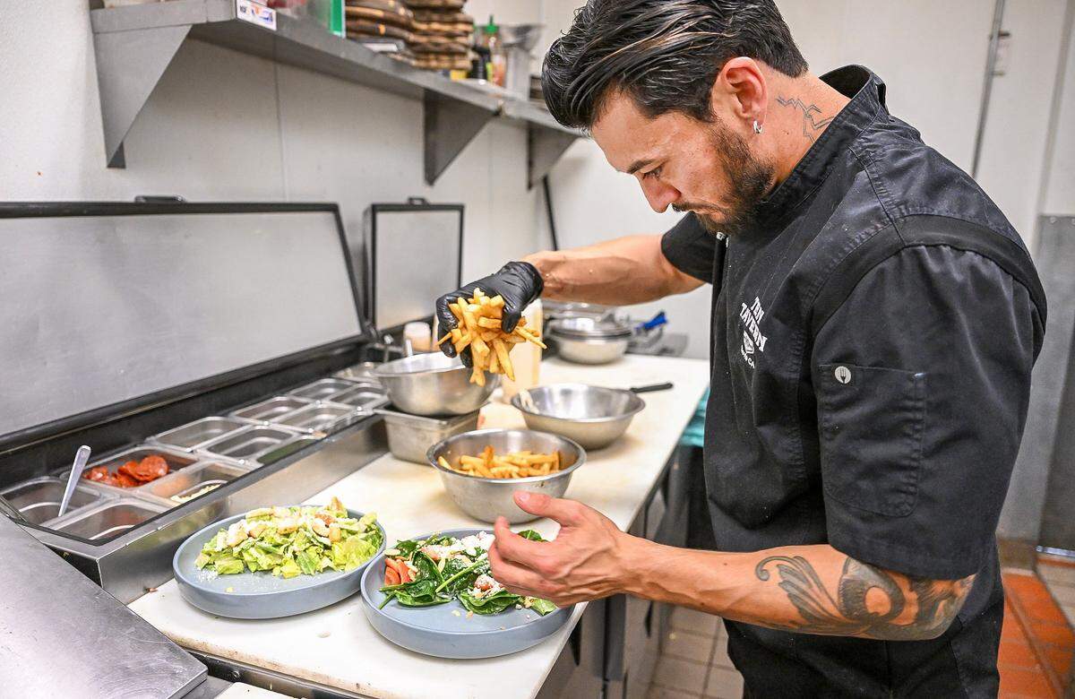 Chef Cory Dutra of Ten Tavern adds french fries to a half a chicken Caesar salad and half a strawberry-spinach salad with chicken as part of the establishment's “girl dinner” menu option.