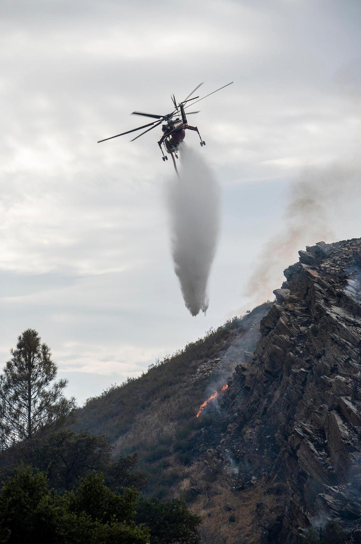 A firefighting helicopter drops water on flames burning along a hillside above Highway 140 in Mariposa County, Calif., on Monday, July 18, 2022.