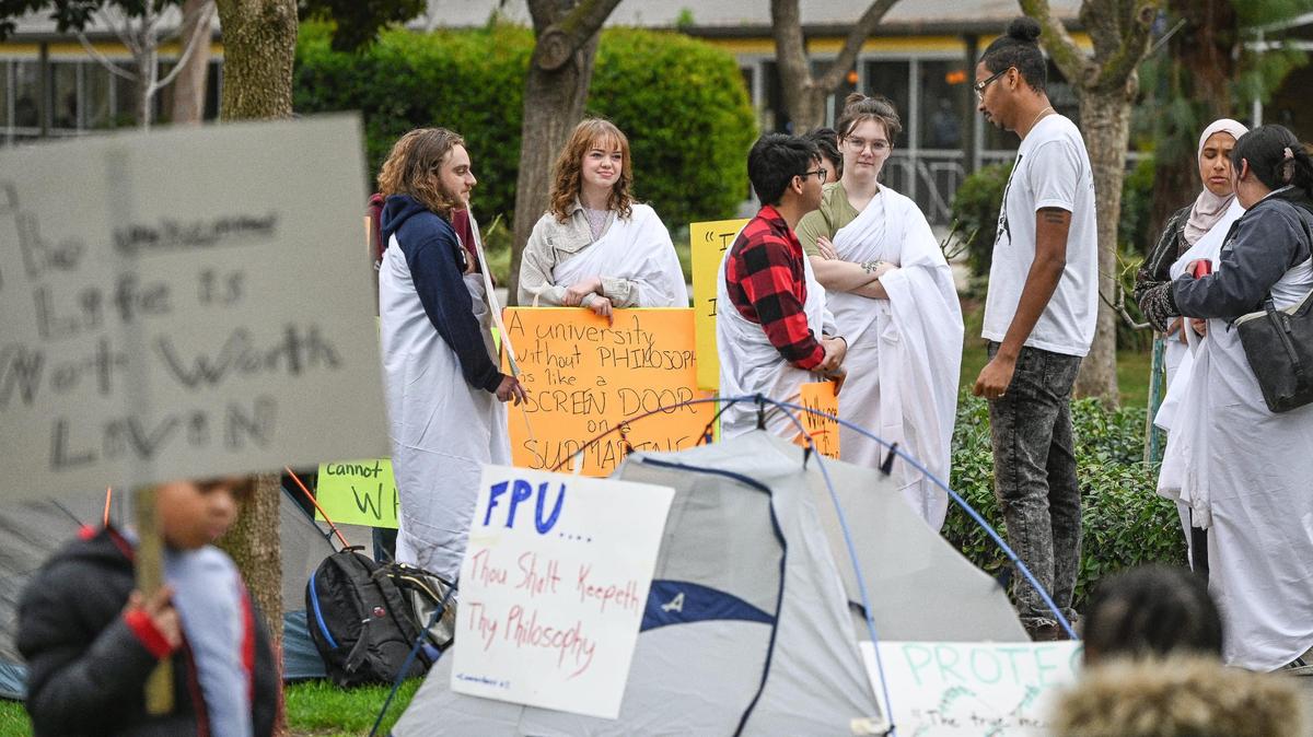 Fresno Pacific University philosophy students and supporters hold signs while wearing togas to protest the laying off of Professor Nathan Carson amid the college’s budget shortfalls outside McDonald Hall on the FPU campus on Wednesday, Jan. 11, 2023. Carson is in charge of both the philosophy dept. and “Summer Sierra Program,” both of which will be cut without him.