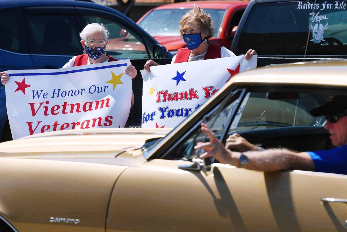 Norma Wallace, top left, and Sandra Dobbs, to the right, both Red Coats VA Ambassadors, stand with posters honoring veterans at a drive through ceremony for Vietnam vets on National Vietnam War Veterans Day on Monday afternoon, March 29, 2021 near Shaw Ave. and 6th Street in Fresno.