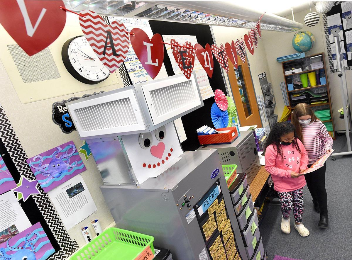 Clovis Elementary School third graders Maysen Hernandez, left, and Kindrey Perry, look over a book next to the HEPA-grade Carrier air filtration unit in their class, decorated for Valentines Day, Feb. 11, 2022. The system is installed in nearly every indoor space in Clovis Unified. Students help decorate the devices, which helps safeguard their health, by decorating them that helps safeguard their health.