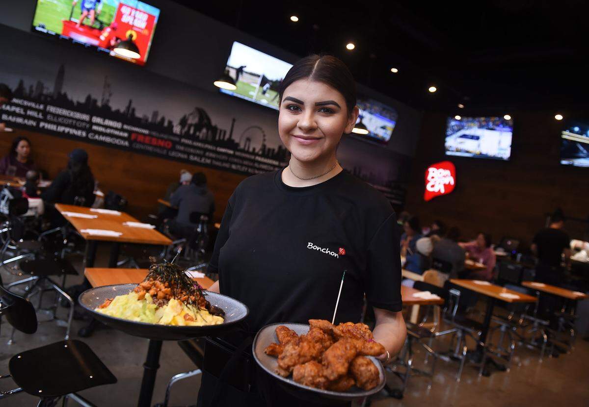 Server Laurissa Martinez holds two entrees available at Bonchon, which has opened a location in Campus Pointe near Fresno State. Photographed Monday, Jan. 28, 2019 in Fresno.