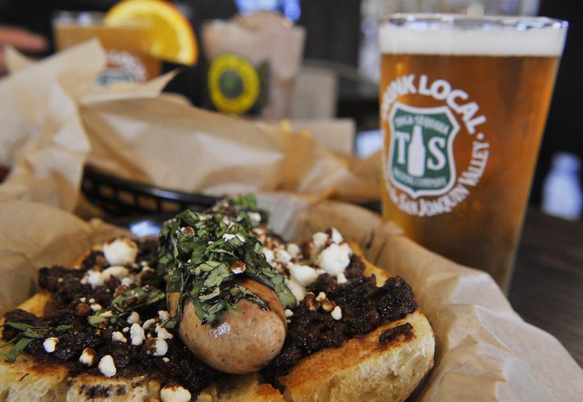 The Napa Dog, with a Tioga-Sequoia beer in the background, is shown at Rocket Dog Gourmet Brats and Brew in Fresno. The eatery, located east of Blackstone on Shaw Avenue, offers brat sandwiches using locally grown ingredients as well as craft beers on tap and in bottle.