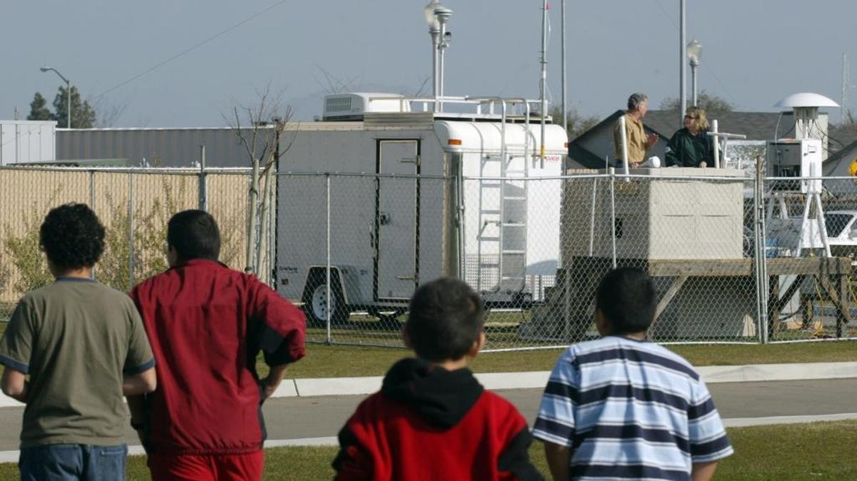 Children play on the school field as staffers from the California Air Resources Board and the Department of Pesticide Regulation take an audit of a toxic sampler set up outside Benevidez Elementary School in Parlier in 2006.