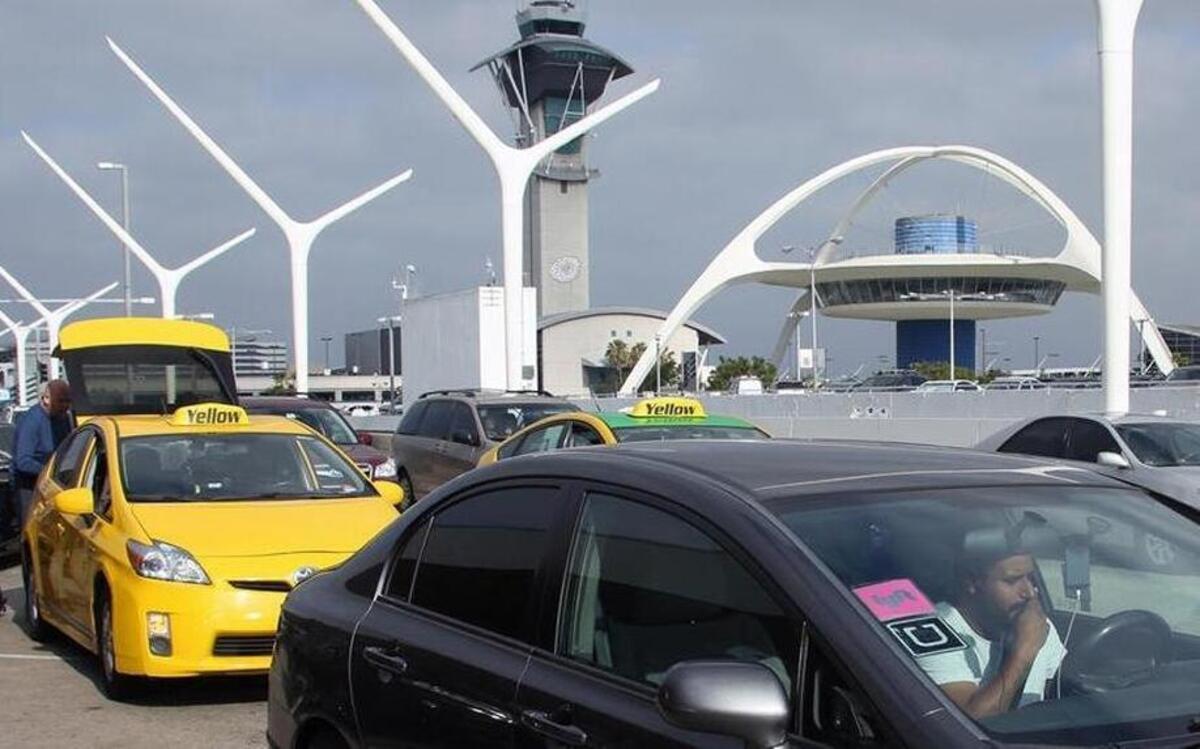 A driver with Uber and Lyft stickers in his front window, right, waits in the taxi line at Los Angeles International Airport to pick up passengers. Fresno Yosemite International Airport has entered into an agreement with ridesharing service Lyft to provide pickup services for travelers.