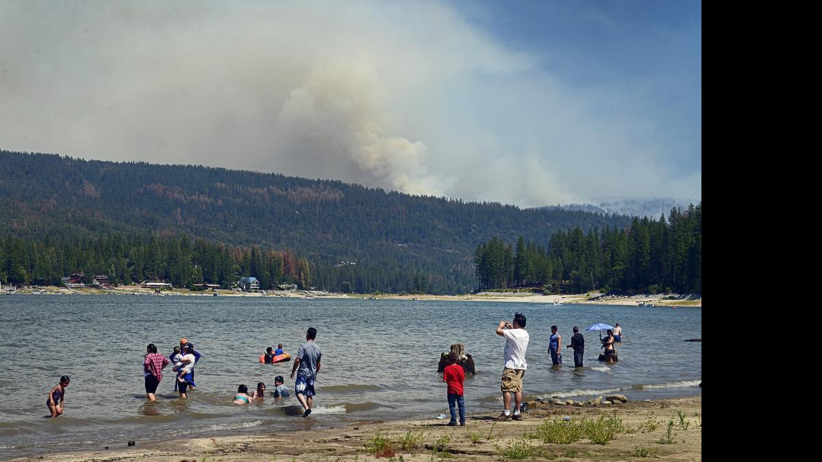 
Vacationers play on the beach at Bass Lake while smoke from the Willow fire billows in the background Sunday. 
