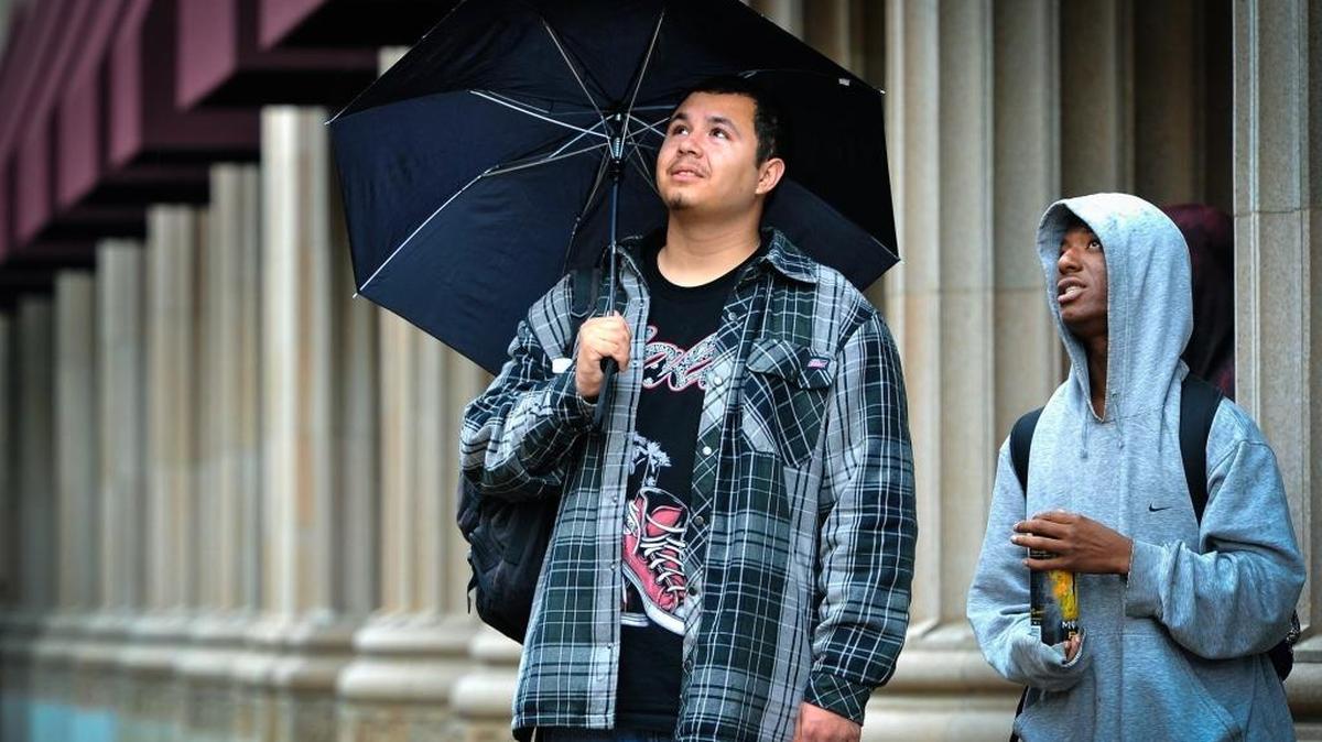 Joseph De La Cruz, left, and friend Nate Cook avoid raindrops and watch the Fresno Fire Department retrieve equipment from the old Security Bank building on the Fulton Mall earlier this November.
