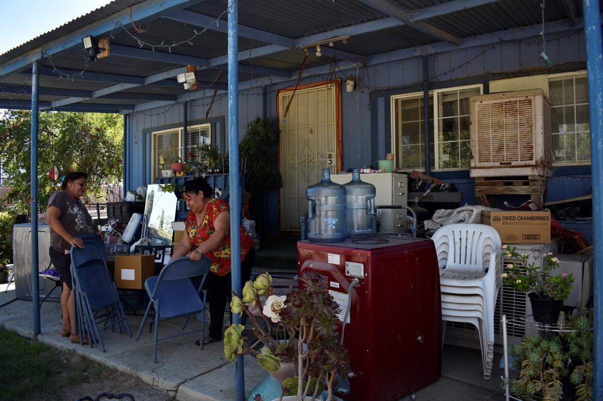 Julia Mendoza, left, and Blanca Gomez, right, wipe the dust off folding chairs at Gomez’s home on Aug. 19, 2022. When they can’t find relief from the heat inside Gomez’s home or on her front porch, the two friends sit under a tree in an abandoned parking lot.