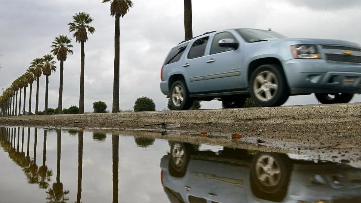 A car drives along Kearney Boulevard west of Fresno Monday, Dec. 28, 2015, where the palm trees and clouds are reflected in a rain water puddle remaining from an earlier storm.