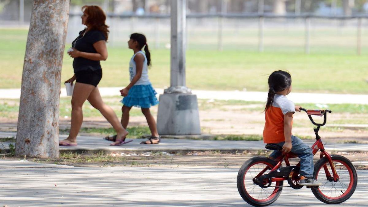 
A mother and daughter walk past a bike-riding girl under shades trees at Holmes Playground in Fresno one day last May. Fresno has tied for last in a new national survey for parks. But the score is an improvement as the city was dead last in 2014. 
