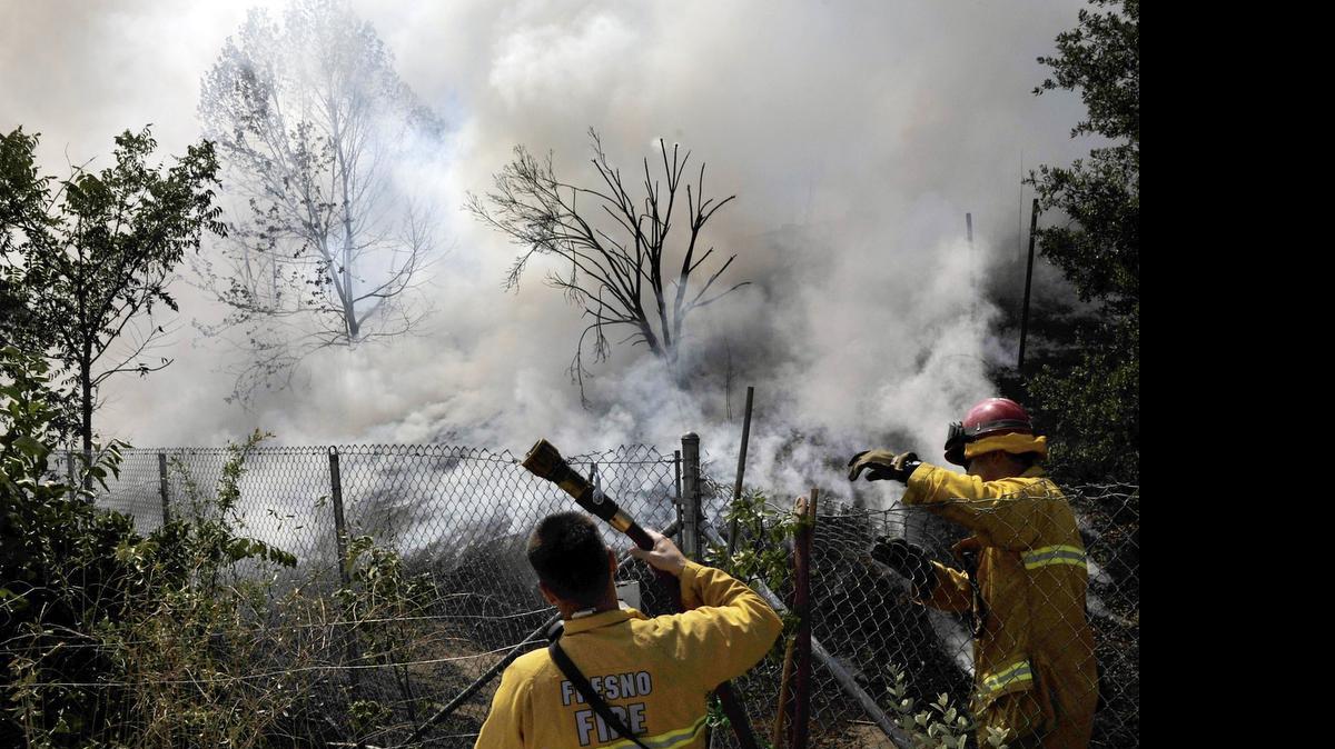 
Firefighters fight a brush fire after it burned down a Highway 180 embankment and through dried brush at East Mildreda Avenue and North Yosemite Avenue Friday, July 3, 2015 in Fresno, Calif.
