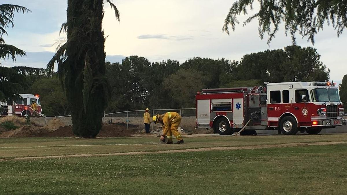 A Fresno firefighter rolls up a water hose at Ararat Cemetery near a brush fire on April 24, 2017.