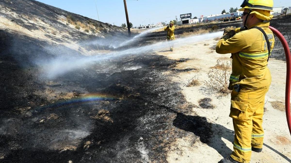 Fresno Fire Department firefighter Rick Osuna puts water on a smoldering grass fire on the Jensen/BNSF rail line overpass Wednesday afternoon, Aug. 10. Fire was of unknown cause, Osuna said.