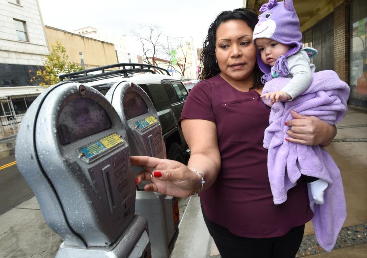 Josephine Smith pone monedas en su parquímetro, con su hija de 10 meses, Mia Castillo, en Fulton Street, en el centro de Fresno, el viernes 15 de febrero de 2019. La ciudad de Fresno está tomando medidas para actualizar los parquímetros existentes en el centro de la ciudad para instalar medidores inteligentes.