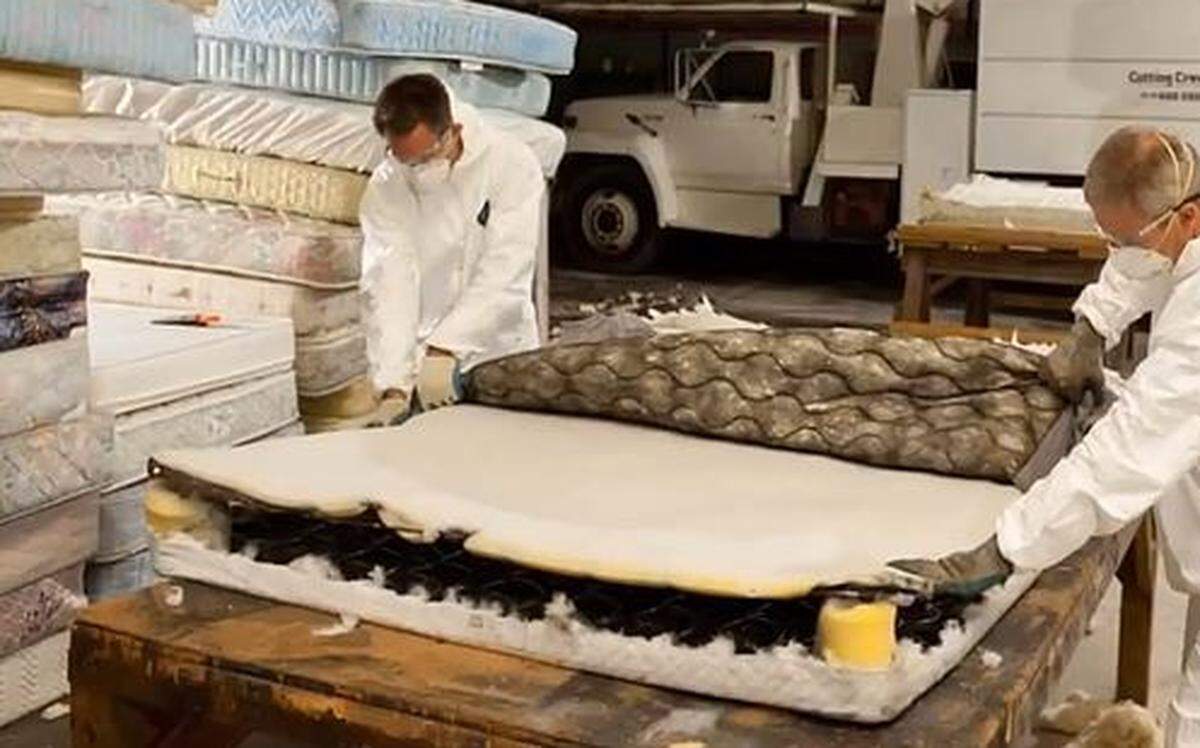 In a photo from the Blue Marble Materials website, a pair of workers cut into a mattress to break it down so that metal springs, foam, fabric and other components can be recycled.