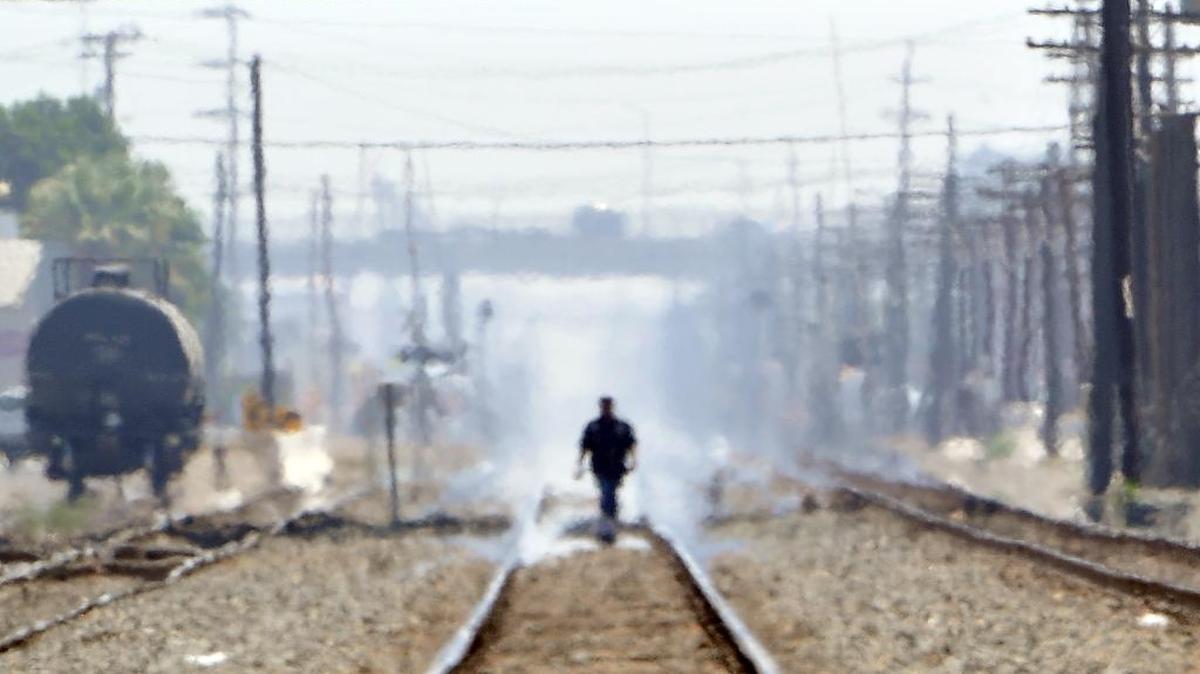 Heat waves distort create a mirage-type appearance of a man walking along the tracks in downtown Fresno, California.