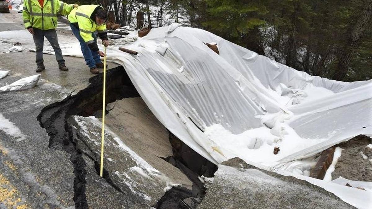 Manuel Aparicio, left, holds the belt of co-worker Lynn Allred of AGEE Construction, as Allred measures the depth of the hole in a section of Highway 41 north of Fish Camp that caved in on Feb 9.
