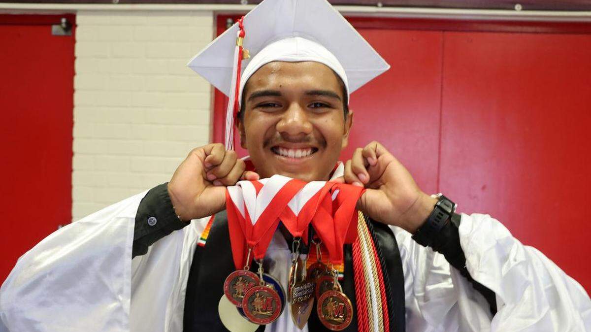 Valedictorian Cristián Avendano Cabrera holds up his stash of medals prior to the McLane High graduation at the school stadium on June 6, 2023.