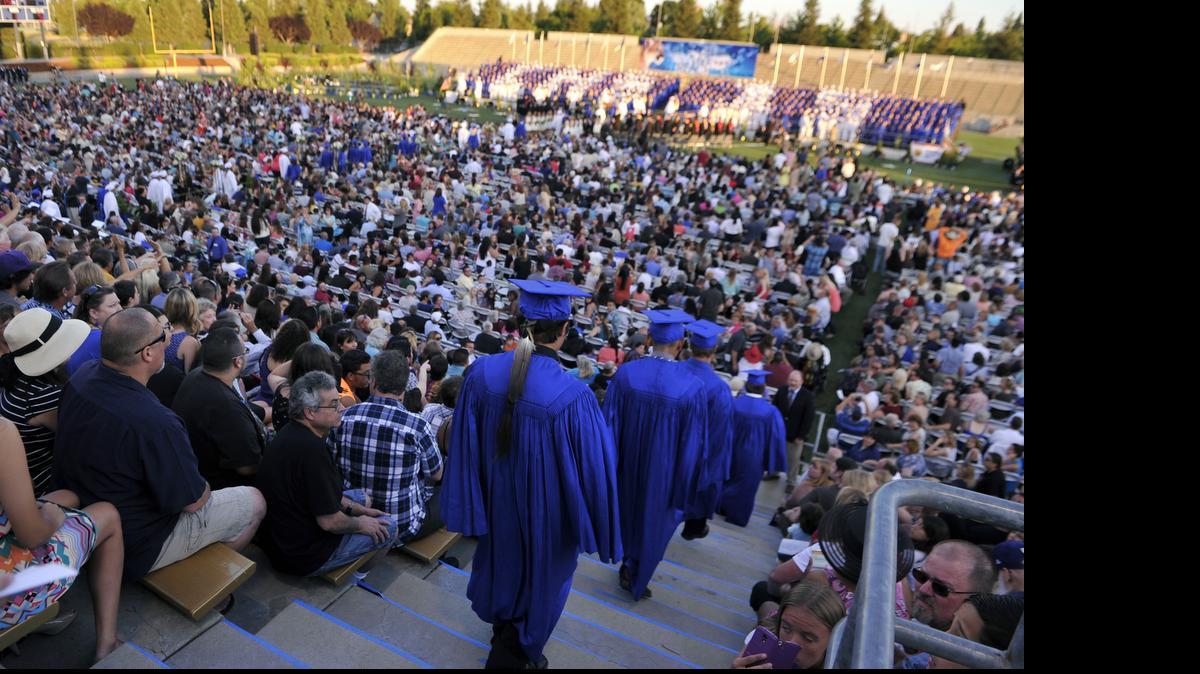
Graduating seniors including Christian Titman, wearing a feather at the end of the line, bottom center, enter Lamonica Stadium for Clovis High's graduation ceremony.
