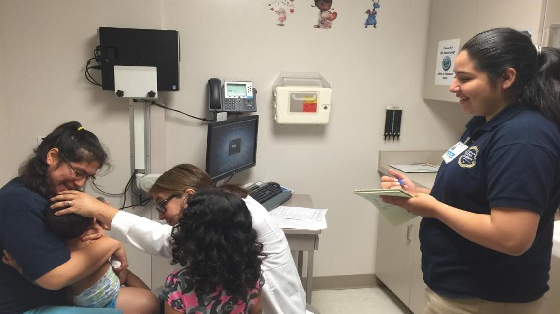 Genesis Benavides, right, observes while Kaiser Permanente Clovis pediatrician Dr. Norma Figueroa examins Jonathan Guerrero in the arms of his mother, Domitila Guerrero.