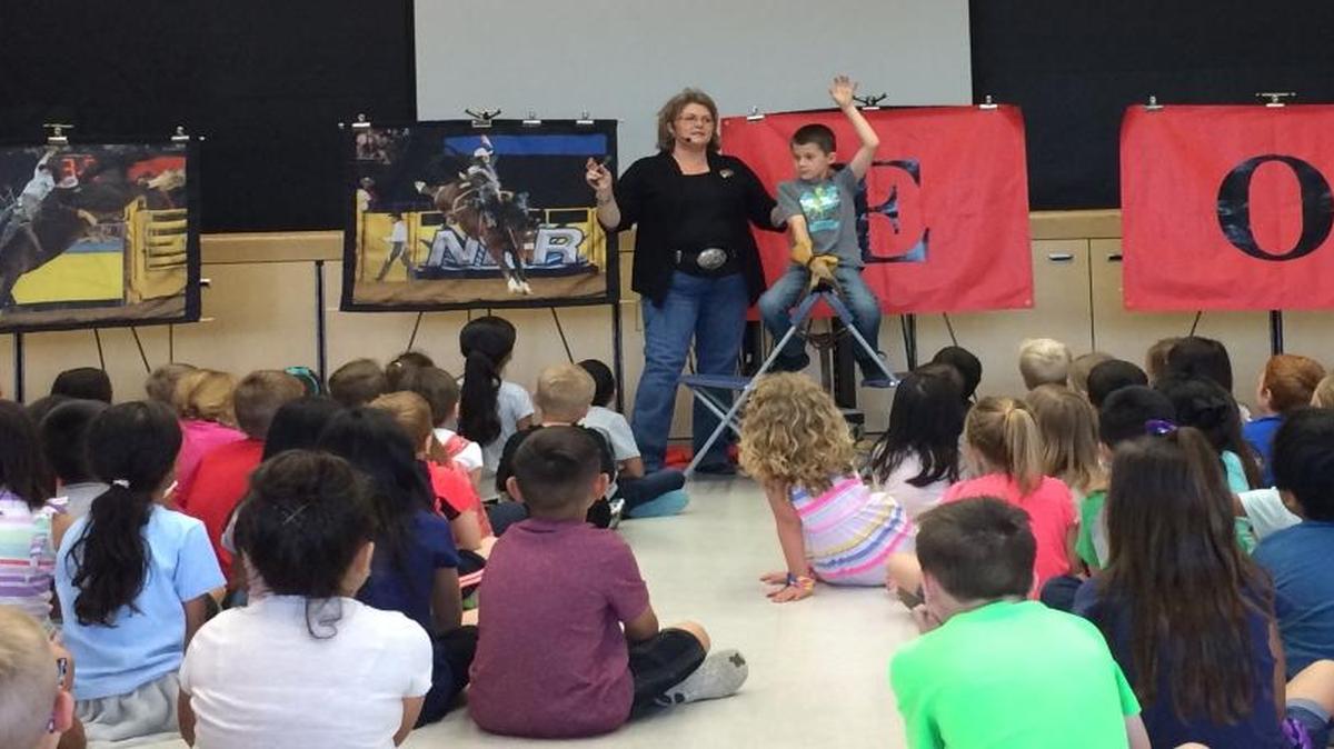 Reagan Elementary first grader Blake Risley imitates saddleback bronc riding as Lemmons explains the rodeo event.