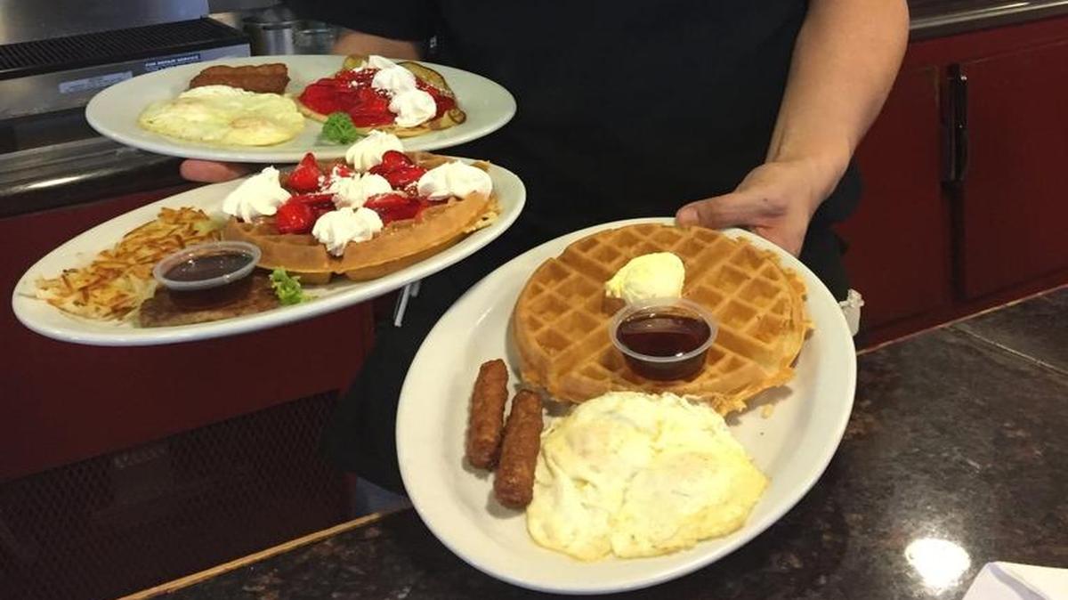 Eddie Mendoza, a server at Old Town Waffle, shows off a Strawberry Waffle combo, a Plain Waffle combo and Strawberry Crepes.