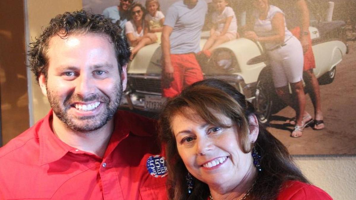 Rhett Williams and his mother, Cheryl Gomes Williams are pictured in the 559 Local Tasting Room in Old Town Clovis. The photo behind them shows the Williams family with the 1956 Chevrolet BelAir that played a part in naming a craft beer after Gomes Williams.