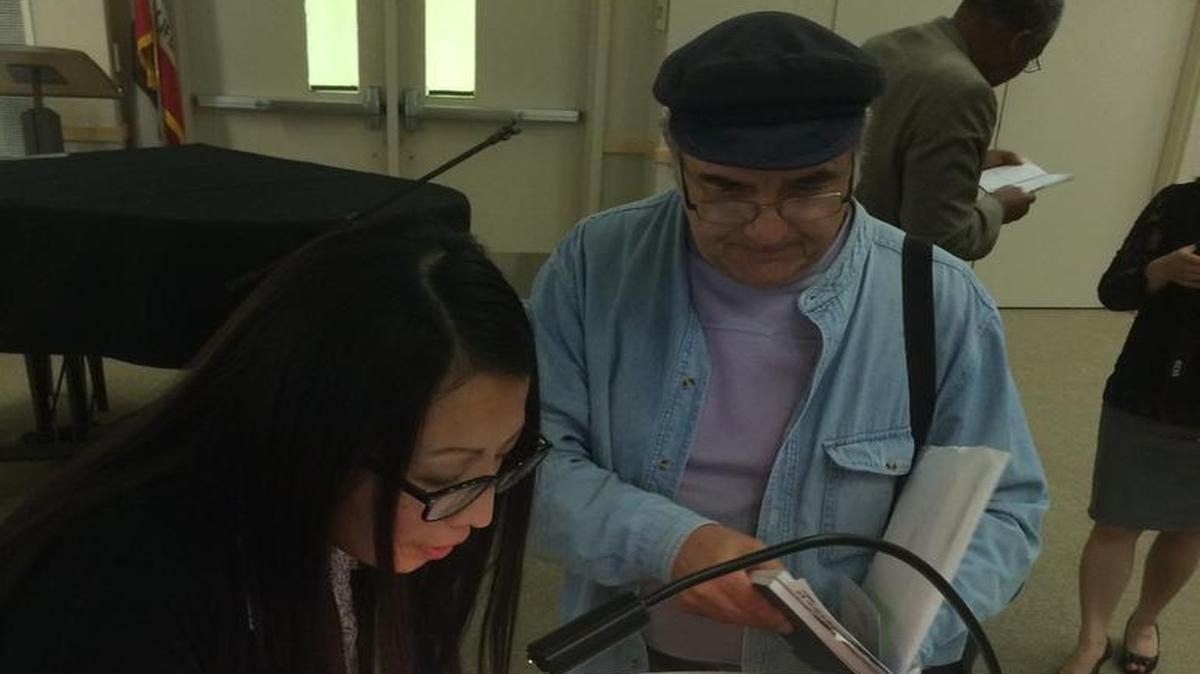 Mai Der Vang signs one of her published poems for poetry reading attendee Leo Pedretti.