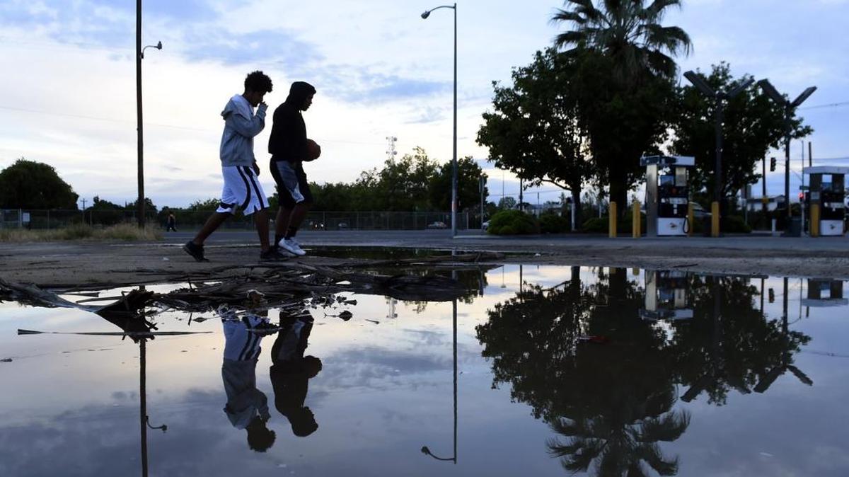 Pedestrians cross standing water in the gutter along Olive Avenue during the annual Tower Classic Car Show held in the Tower District on Saturday, April 9, 2016 in Fresno, Calif. Early Saturday rain subsided by mid-morning, although the National Weather Service predicts a chance of showers continuing through Monday night.