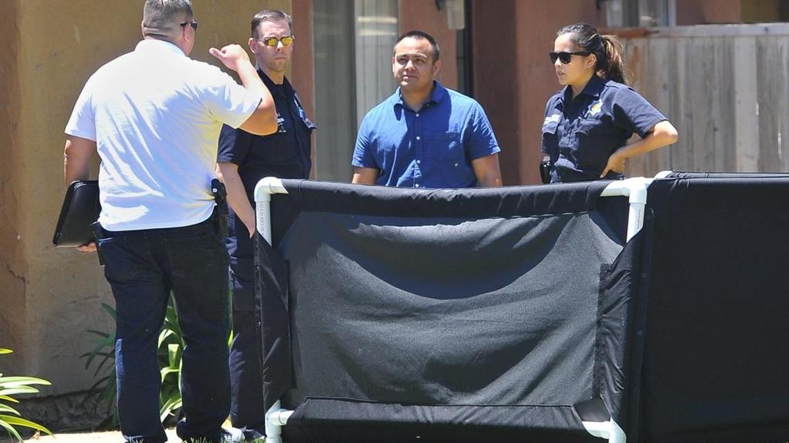 A privacy screen shields a deceased person from view as Fresno Police CSI members and a detective, left, gather at the scene in front of an apartment where two people and a dog were shot to death, Friday afternoon on Marks Avenue.