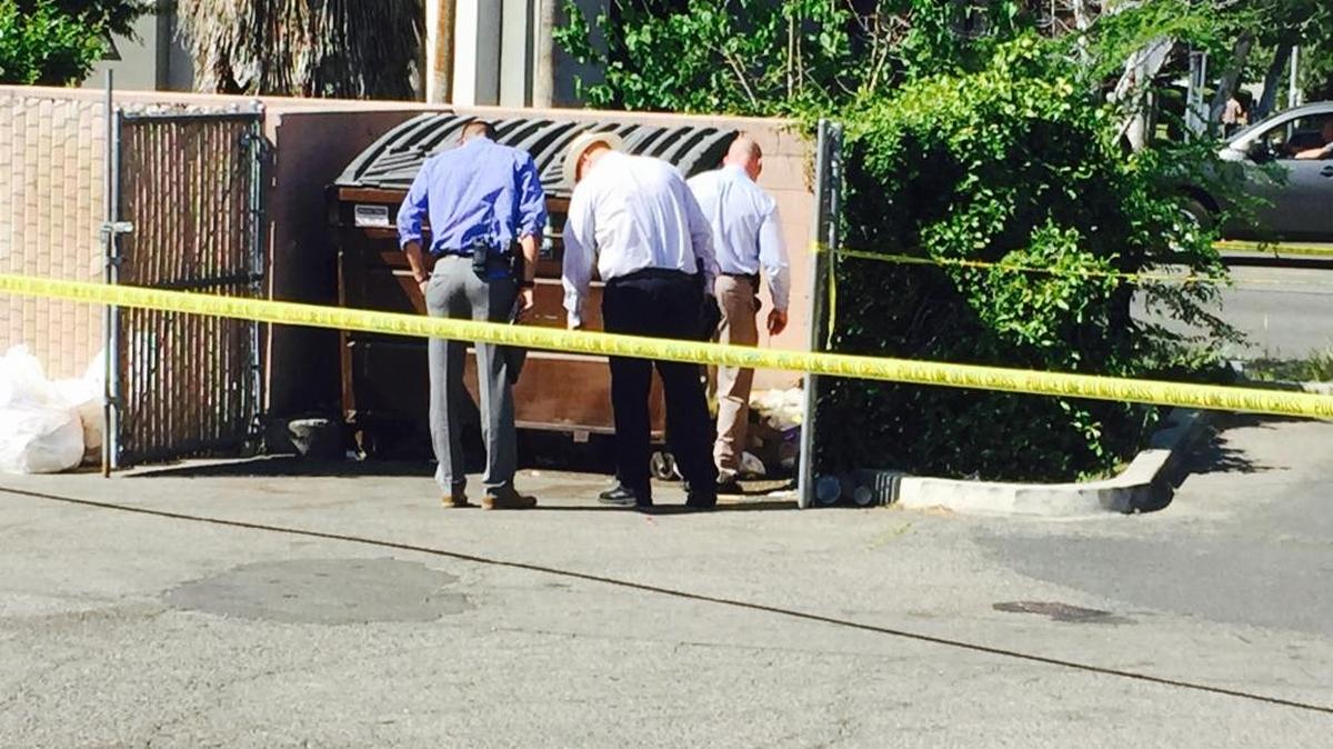 Fresno police detectives search around the dumpster where a male body was found. The scene is behind a Starbucks at Fresno and U streets.