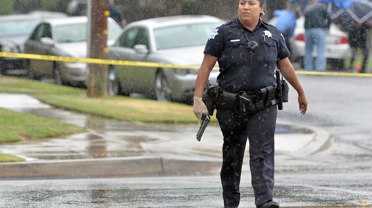 A Fresno police officer carries a weapon away from where a body lays after two people were shot at on Thursday, Oct.1, 2015 at North San Pablo Avenue and East Barstow Avenue in Fresno.