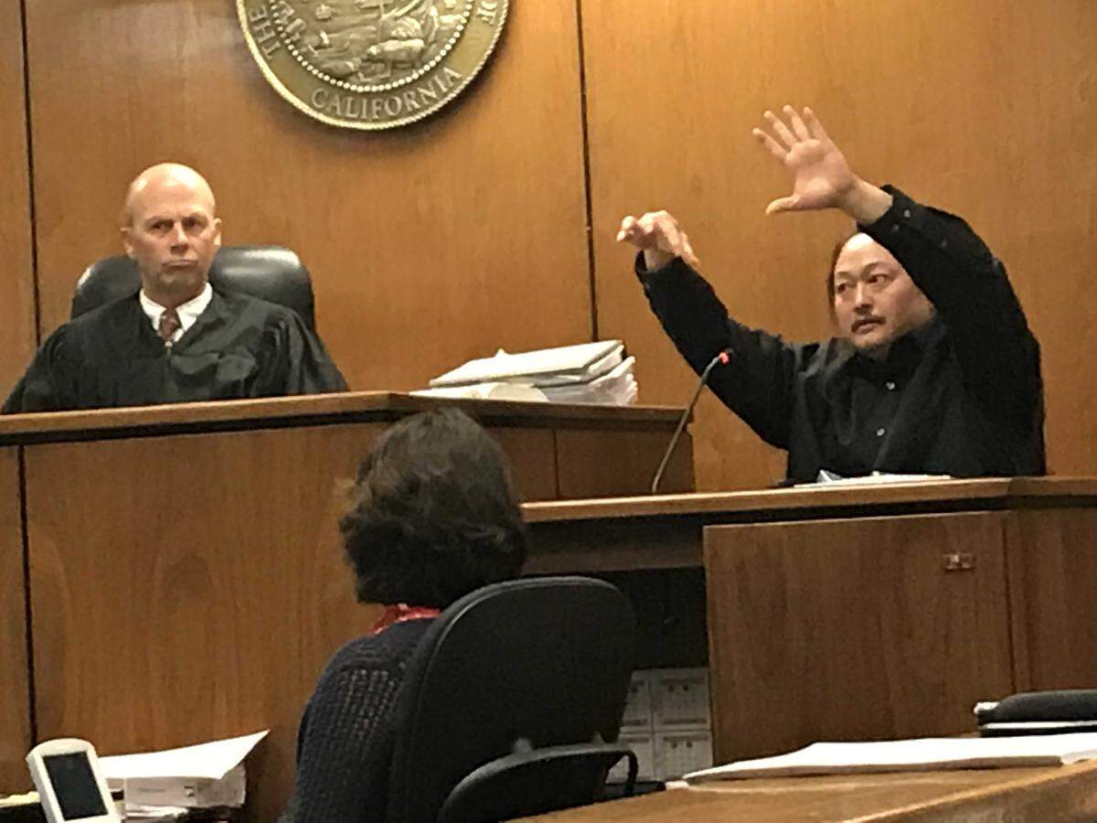 From the witness stand, Thong Vang shows a Fresno Superior Court jury on Thursday, March 22, 2018, how he surrendered to law enforcement by holding one arm up and pinching a gun with his fingers. Also pictured is Judge Timothy Kams. Vang, 38, of Fresno, is on trial, accused of wounding two correctional officers inside the mail Fresno County Jail in September 2016.