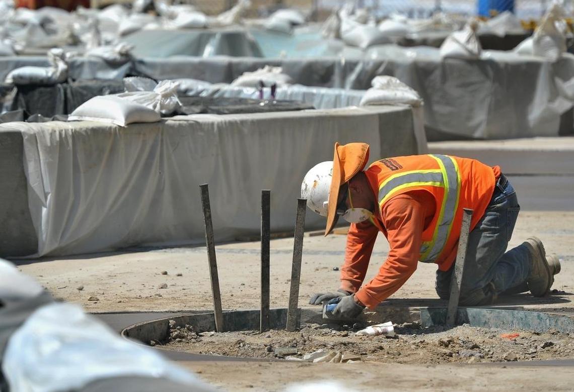 A concrete worker does some finish work on a planter curbing on Merced Street amid a maze of walls of a water feature covered with plastic as it cures in the heat during the construction project on the Fulton Mall Wednesday morning.