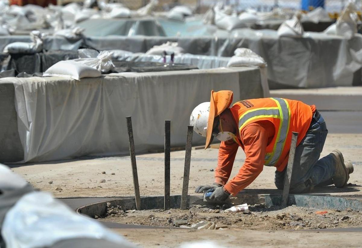 A concrete worker does some finish work on a planter curbing on Merced Street amid a maze of walls of a water feature covered with plastic as it cures in the heat during the construction project on the Fulton Mall Wednesday morning.