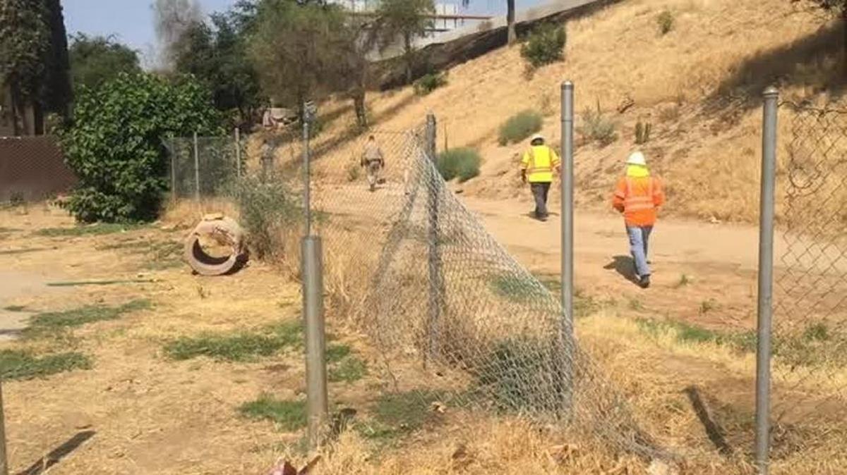 Caltrans workers walk along a fence that has been cut by homeless people. The state agency this week is in the processing of removing homeless encampments along highways in the Fresno-Clovis area.
