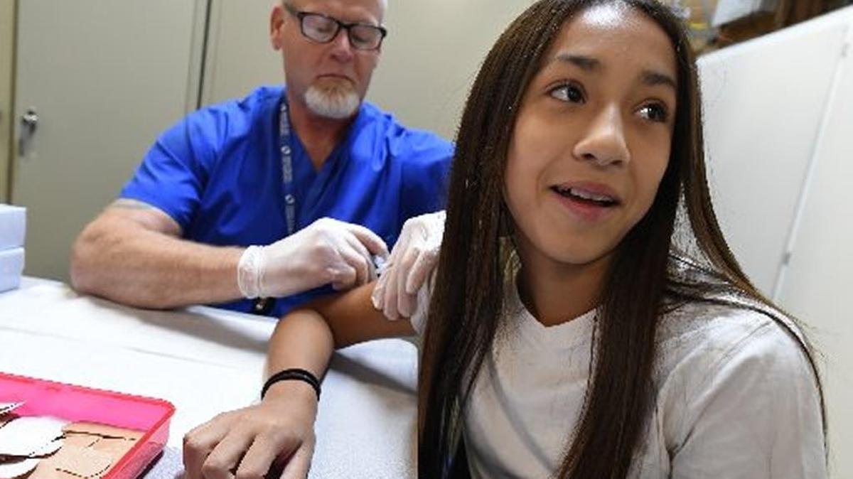Fresno Unified student Yahiara Morillo puts on a brave face for her back-to-school vaccination administered by nurse Gordon Cromwell in August. The district is looking to create several school-based health centers for community use.
