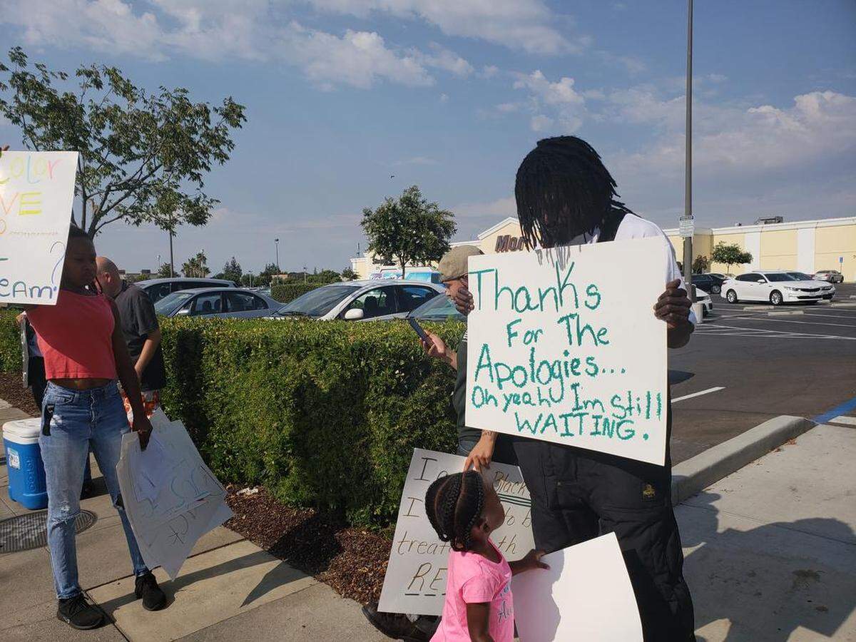 Dorian Johnson looks at his daughter as they hold signs outside the northeast Fresno T-Mobile store where Johnson was made to crawl across the cement and detained by police after a false robbery call that he says was based on his skin color.