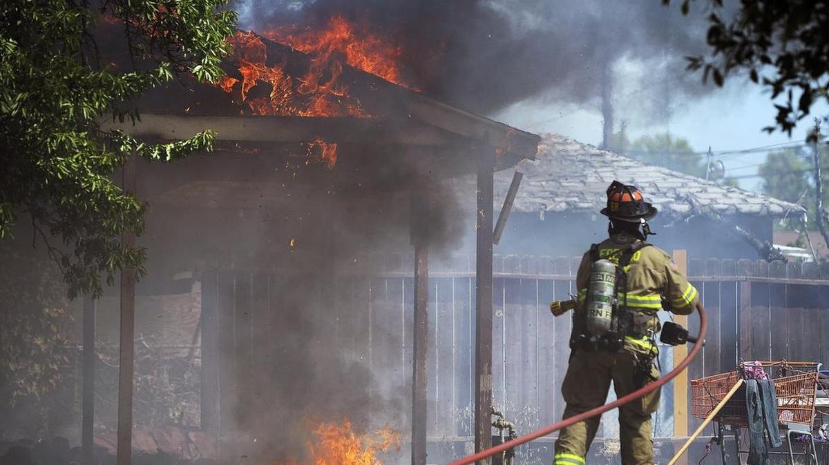 A firefighter prepares to douse a carport on fire at 436 Fresno St. on Tuesday afternoon, July 4, 2017 in Fresno, Calif.