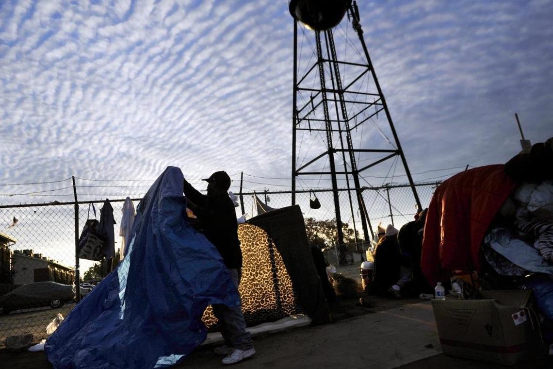 A man sets up a tarp along a sidewalk in Fresno in 2015. The city of Fresno is considering stricter limitations on where the homeless can set up camp, arguing that the measures are necessary for public safety and ADA compliance.