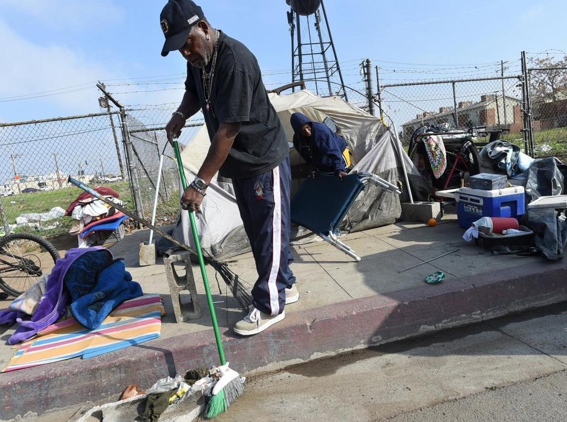 Patrick Brown sweeps up the gutter in front of the tent on F Street that he shares with wife, LaTanya, in background, as they tend to the task of setting back up their shelter. They, like other homeless people on F Street, take down their tents, move, then set them back up.